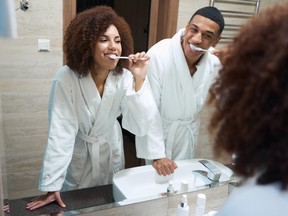 Man and a woman brush their teeth together in front of a mirror.