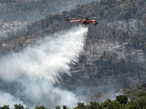 A firefighting helicopter drops water over a wildfire