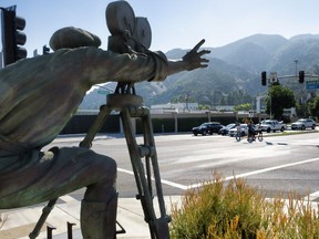 With a statue of a cameraman in the foreground, SAG-AFTRA picketers carrying signs cross a street near the gates of Warner Bros. studios in Burbank, Calif., Tuesday, Sep. 26, 2023.