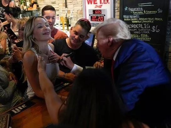 ‘OH MY GOD:’ Donald Trump signs woman’s tank top, dishes out slices during campaign stop