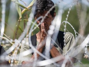 A migrant from Venezuela prays as he waits for U.S. Border Patrol agents to cut the razor wire after he crossed the Rio Grande to Eagle Pass, Texa