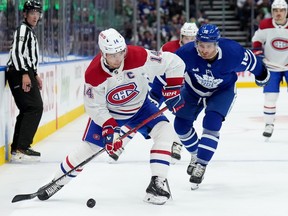 Montreal Canadiens centre Nick Suzuki (14) moves the puck down ice under pressure from Toronto Maple Leafs centre Max Domi.