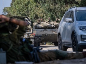 An IDF soldier rests while a tank moves past him