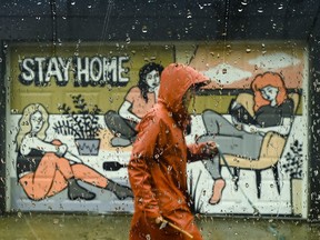 A person walks past a COVID-19 mural designed by artist Emily May Rose on a rainy day during the COVID-19 pandemic in Toronto on Monday, April 12, 2021.