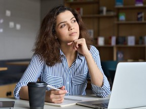 Young woman looks off into the distance while working on a laptop in an office