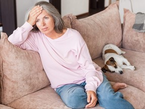 Sad pensive middle age woman looking down depressed sitting on the sofa