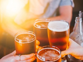 Beer glasses raised in a toast. Close-up hands with glasses. Blurred bar interior at the background.