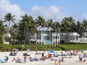Beachgoers on sandy white beach in front of grand estates in Naples, Florida.