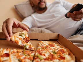 Closeup of adult man taking slice of pizza while enjoying lazy weekend at home