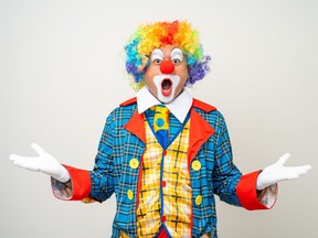 A man dressed as a clown in colourful costume wearing wig.