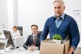 Aging employee carries a box of his belongings while leaving the office after being terminated.