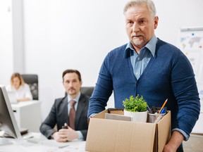 Aging employee carries a box of his belongings while leaving the office after being terminated.