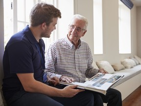 Senior man sitting looking at photo album with a young man