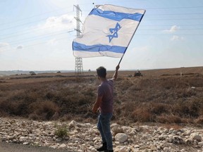 A man waves the Israeli flag across from Israeli army positions near the border area with Gaza on Wednesday, Oct. 11, 2023.