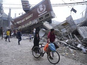 Palestinians walk by the destroyed building of Al Nuseirat Bakery in an Israeli airstrike Nusseirat refugee camp Gaza Strip, Wednesday, Oct. 18, 2023.