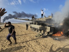 Palestinians celebrate by a destroyed Israeli tank at the Gaza Strip fence east of Khan Younis southern Saturday, Oct. 7, 2023.