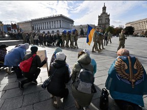 Protesters draped in flags and holding placards of Ukrainian prisoners of war and missing servicemen kneel during a funeral service for a fallen soldier, at Independence Square in Kyiv on Oct. 16, 2023, amid Russian invasion in Ukraine.
