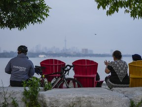 People sit along the waterfront at Humber Bay Park in Toronto, June 28, 2023. Ontario's natural resources and forestry minister says the government will spend an additional $20.5 million over three years to help fight wildfires.