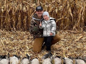 Man and son posing behind row of dead geese