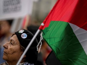 reading "Free Palestine" and "Peace Yes War No" as she holds a Palestinian flag during