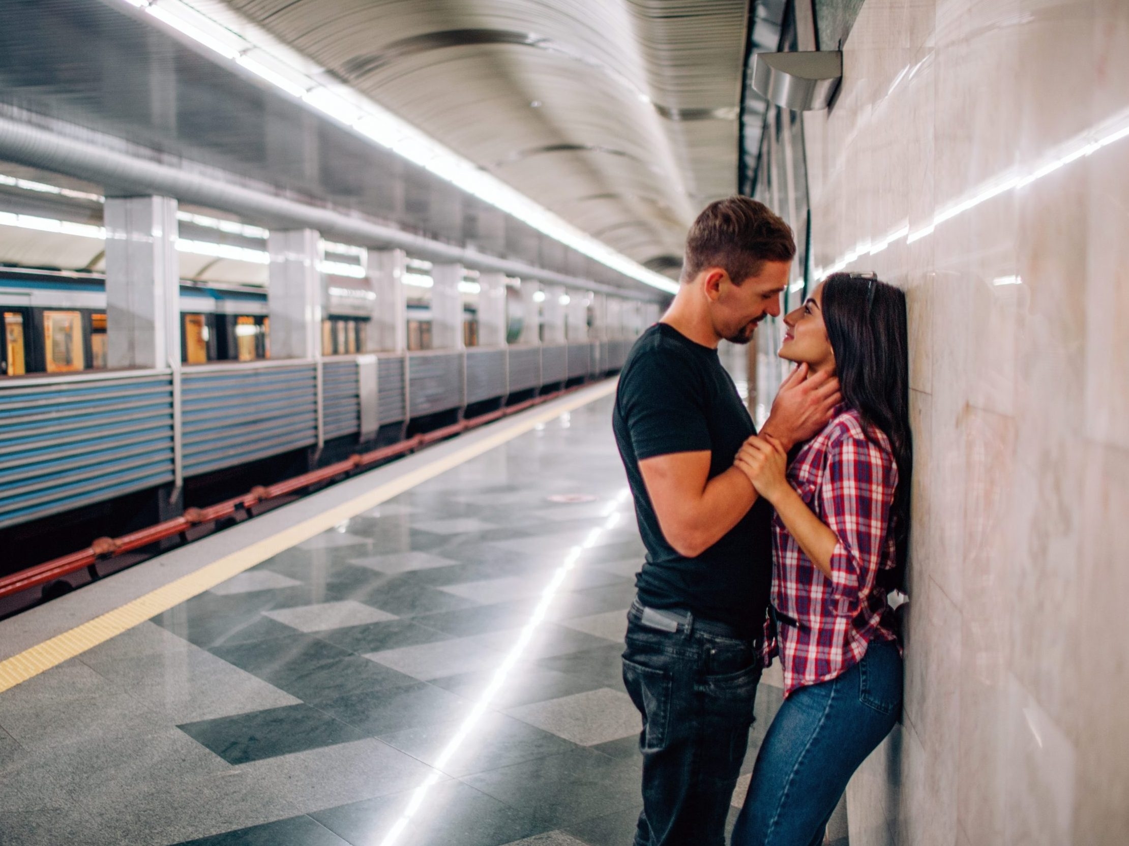 Young man and woman use underground. Couple in subway. Cheerful paasionate people lean to wall. kissing time. Guy hold hand on her neck. Love story. Modern urban view.