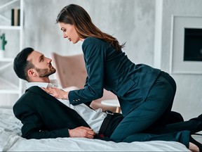 Man and woman in suits on bed about to get intimate.