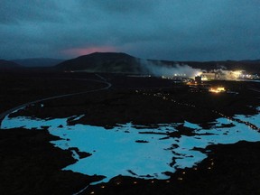The red shimmer from magma is seen coming out from the erupting Fagradalsfjall volcano behind the tourist land mark Blue Lagoon, near the town of Grindavik some 40 km west of the Icelandic capital Reykjavik, on March 20, 2021.