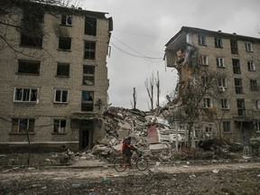A man rides his bicycle in front of a destroyed apartment building