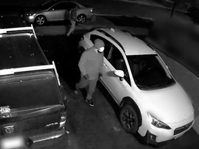 Masked person by a white car on a driveway at night
