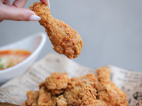 Hand pulling chicken drumstick from pile of fried chicken.