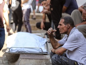 A Palestinian man smokes a cigarette as he sits next to a covered body outside a hospital following Israel's bombardment of Gaza City's eastern suburb of Shujaiya on Nov. 4, 2023, amid the ongoing battles between Israel and the Palestinian group Hamas.