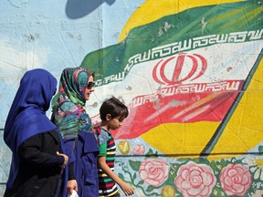 Iranian women walk past a mural