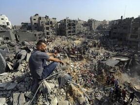 A man sits on the rubble overlooking the debris of buildings