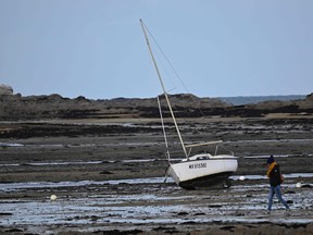 A woman walks past a boat on the foreshore at low tide