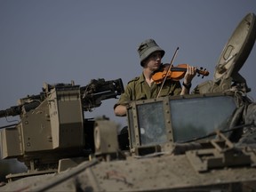 An Israeli soldier plays a violin in an armoured vehicle near the border of the Gaza Strip, Monday, Dec. 18, 2023.