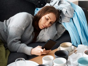 Shot of a young woman lying on her messy couch looking depressed and using her smartphone