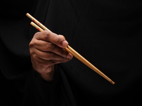 Asian male dark skinned single hand fist finger on black background holding chopsticks feed eat
