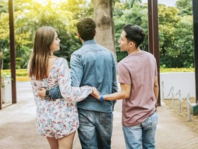 Unfaithful girl walking in the park with her boyfriend while holding another man hand. Love triangle concept. Woman holding hands with another man while walking with her boyfriend outdoor