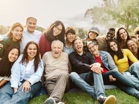 Happy multigenerational people having fun sitting on grass in a public park