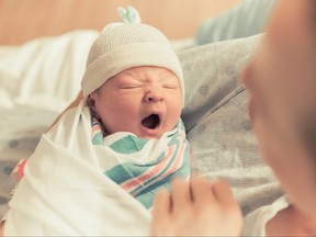 Yawning newborn in swaddle being held by mother.