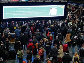 Rail travellers stand beneath an electronic information board displaying a message from Network Rail about damaged overhead wires leading to suspended services, at Euston Station in London on Dec. 21, 2023, as services are disrupted due to damage caused by strong winds.
