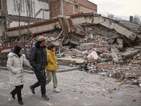 People walk past a collapsed building after an earthquake in Dahejia, Jishishan County in northwest China's Gansu province on Dec. 19, 2023.