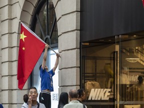 An employee adjusts Chinese flag outside a Nike store on Nanjing East Road, one of the city's main commercial and tourist area, in Shanghai, China, on Saturday, Sept. 30, 2023.