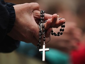 A woman holds rosary beads while she prays