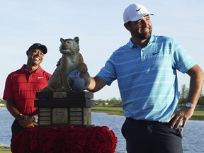 Scottie Scheffler poses with the Hero World Challenge PGA Tour trophy as Tiger Woods smiles in the background.