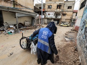 A man collects trash while wearing a jacket bearing the logo of the United Nations Relief and Works Agency for Palestine Refugees in the Near East (UNRWA), along a street in the city of Jenin in the occupied West Bank on Jan. 30, 2024.