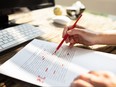 Close-up of a person's hand marking errors with red marker.