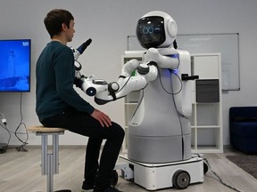 An employee sits in front of the white-coloured "humanoid" Garmi in the laboratory of the Research Center Geriatronics of the Technical University Munich, in Garmisch-Partenkirchen, southern Germany, on March 6, 2023.