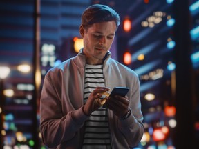 Man walking in city at night looking at smartphone.