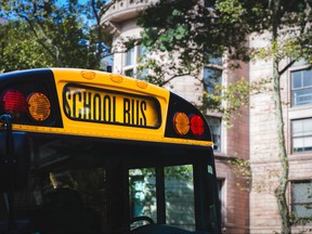 A close up of the front end of a traditional American yellow school bus outside an elementary school.